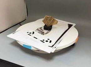 Photograph of a ceramic fragment propped on a black sponge block and sitting on a white, electrical turntable in a photographic light box, as described in the text.